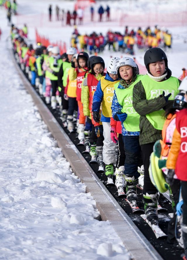 在吉林北大壶滑雪场,吉林市第二实验小学学生们在滑雪教练的带领下乘坐“魔毯”前往雪场学习区域。